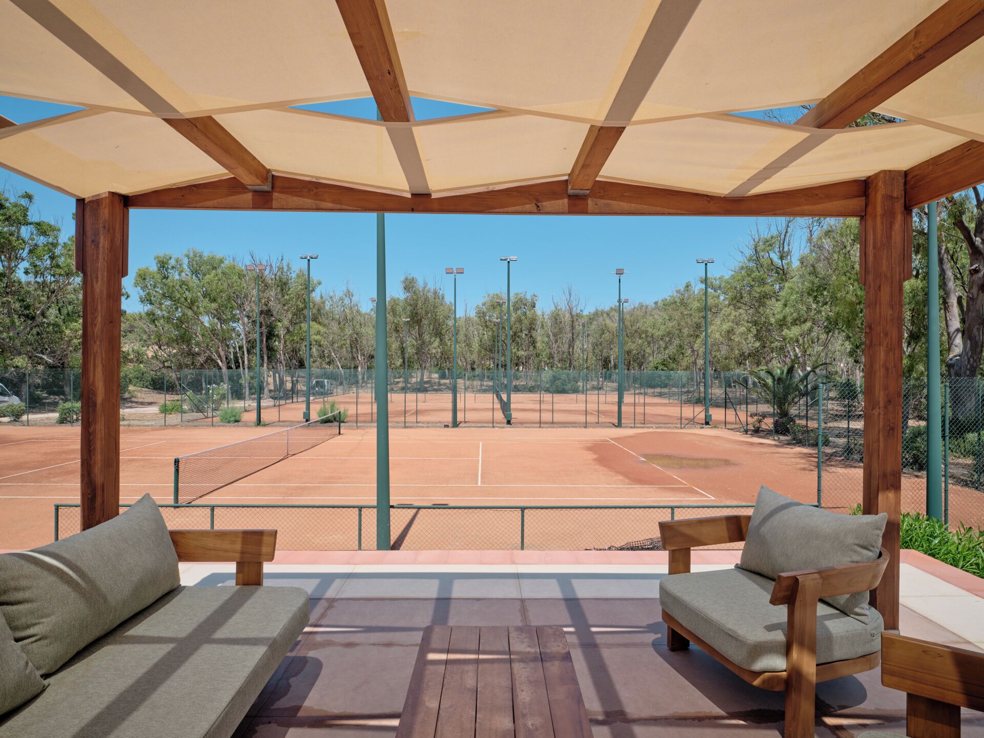 A tennis court with a covered seating area and a view of the surrounding trees.