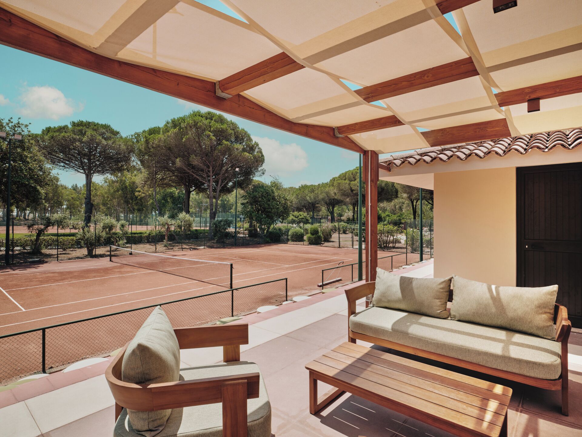 Zona relax all'aperto con campo da tennis, mobili in legno e un pergolato.