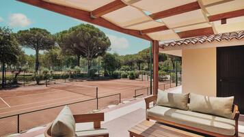 Zona relax all'aperto con campo da tennis, mobili in legno e un pergolato.