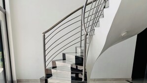 A modern staircase with a metal railing and black steps, leading to a landing with a glass door.