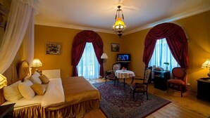 A hotel room with a bed, a desk, a chair, a television, and a chandelier. - SPA Hotel Mārcienas Muiža (Mārciena)