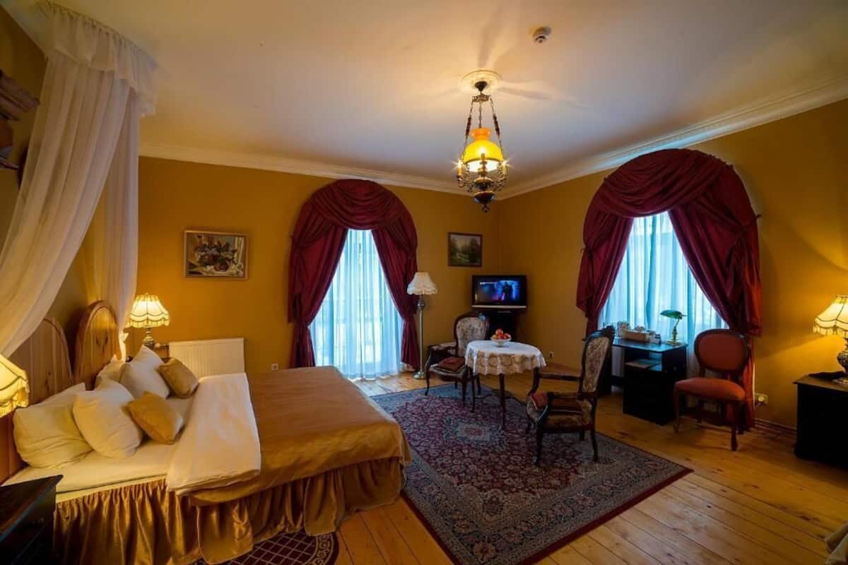 A hotel room with a bed, a desk, a chair, a television, and a chandelier.