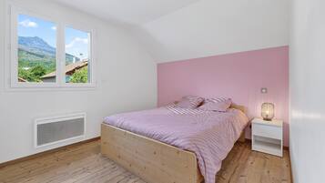 A bedroom with a wooden bed, a nightstand, a window with a view of mountains, and a pink wall.
