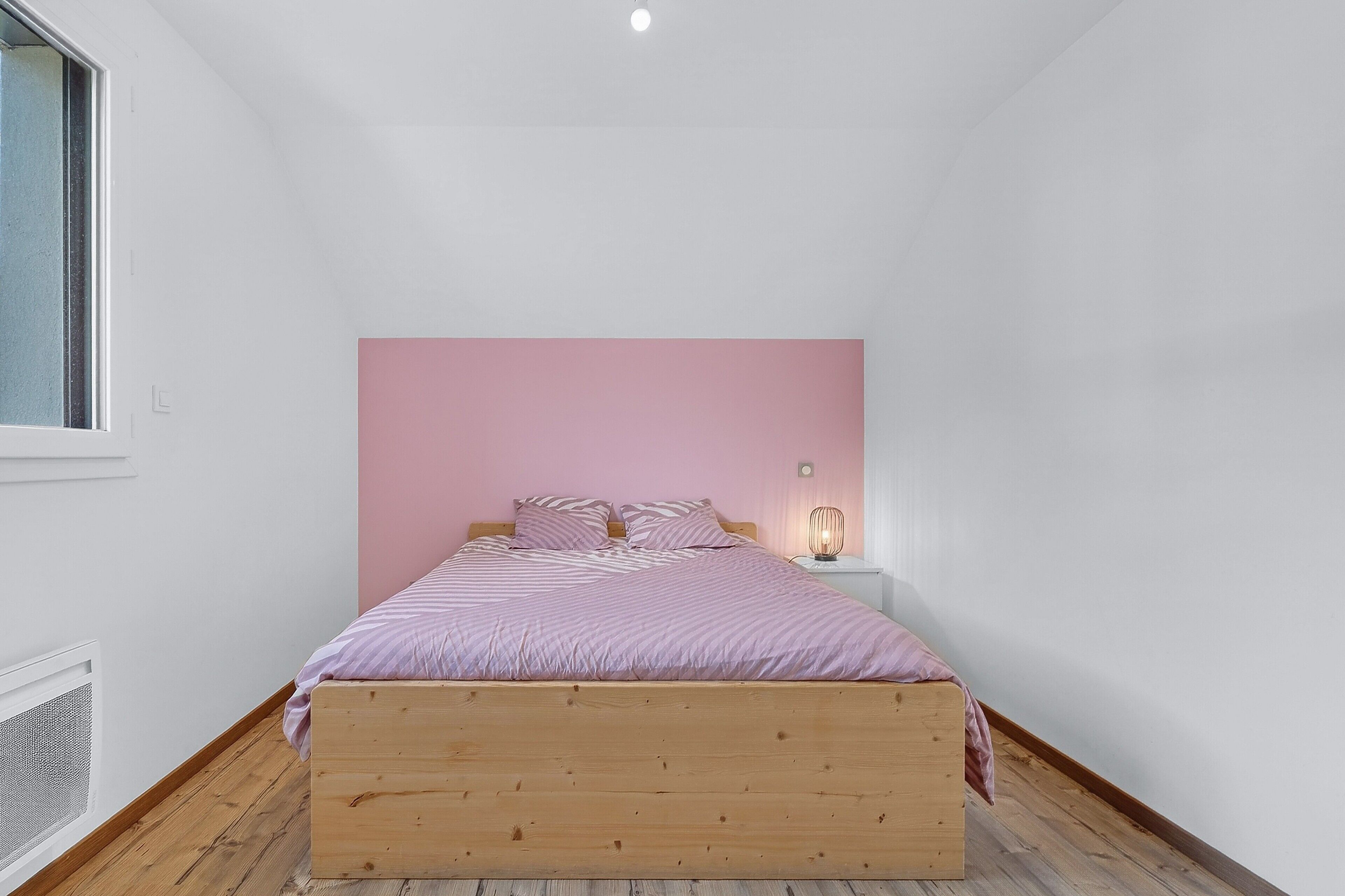 Ein Schlafzimmer mit einem hölzernen Bett, einer pinkfarbenen Kopfteil und einer Nachttischlampe.