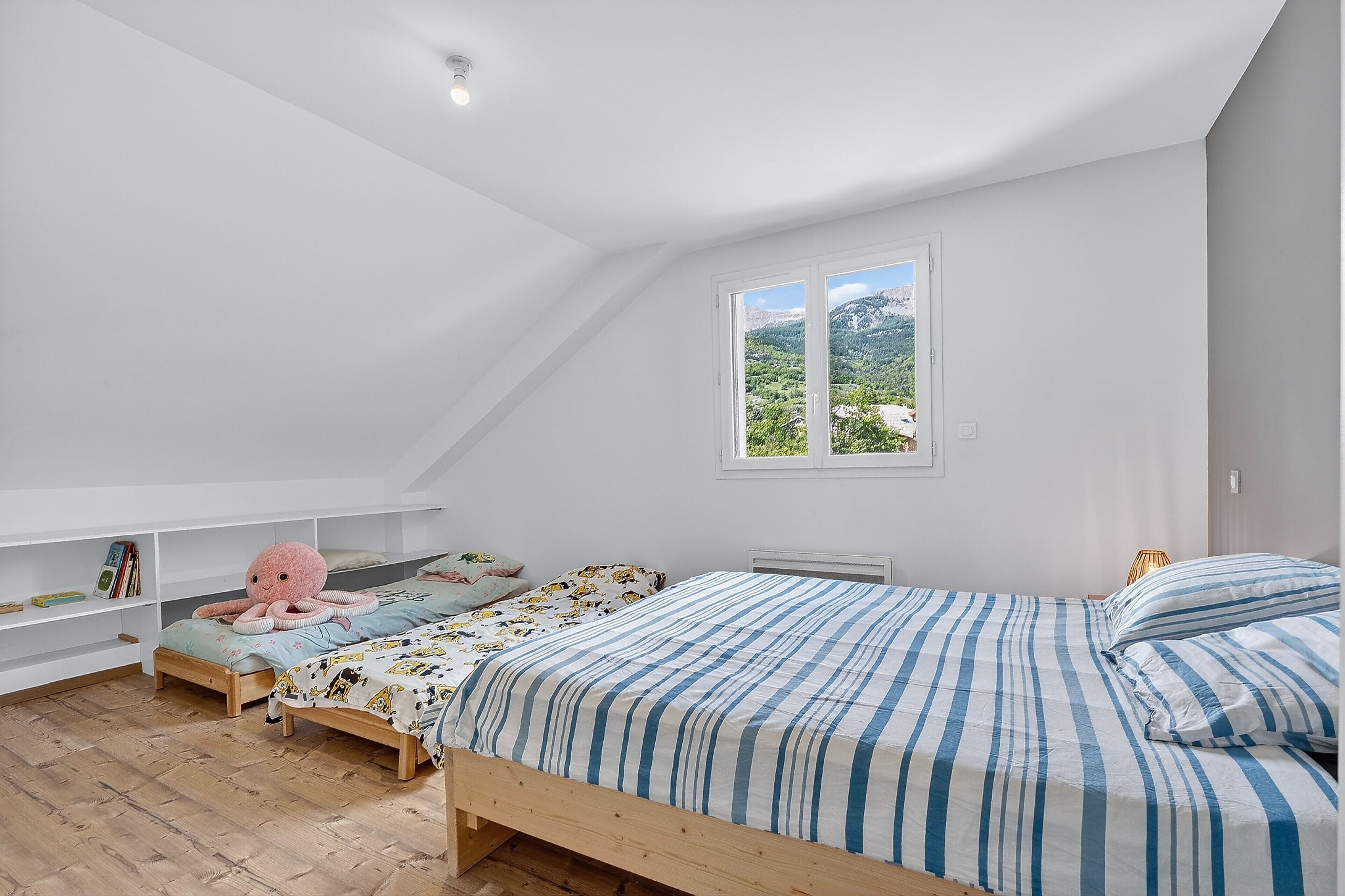 Een slaapkamer met twee bedden, een groot raam, een plafondlamp en een houten vloer.