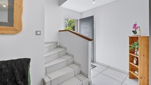 Una escalera con baldosas blancas, barandilla de madera y una estantería de madera con plantas.
