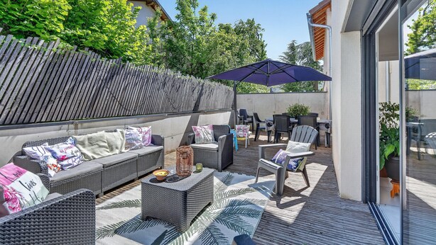 Un patio exterior con un sofá, sillas, una mesa y una sombrilla.