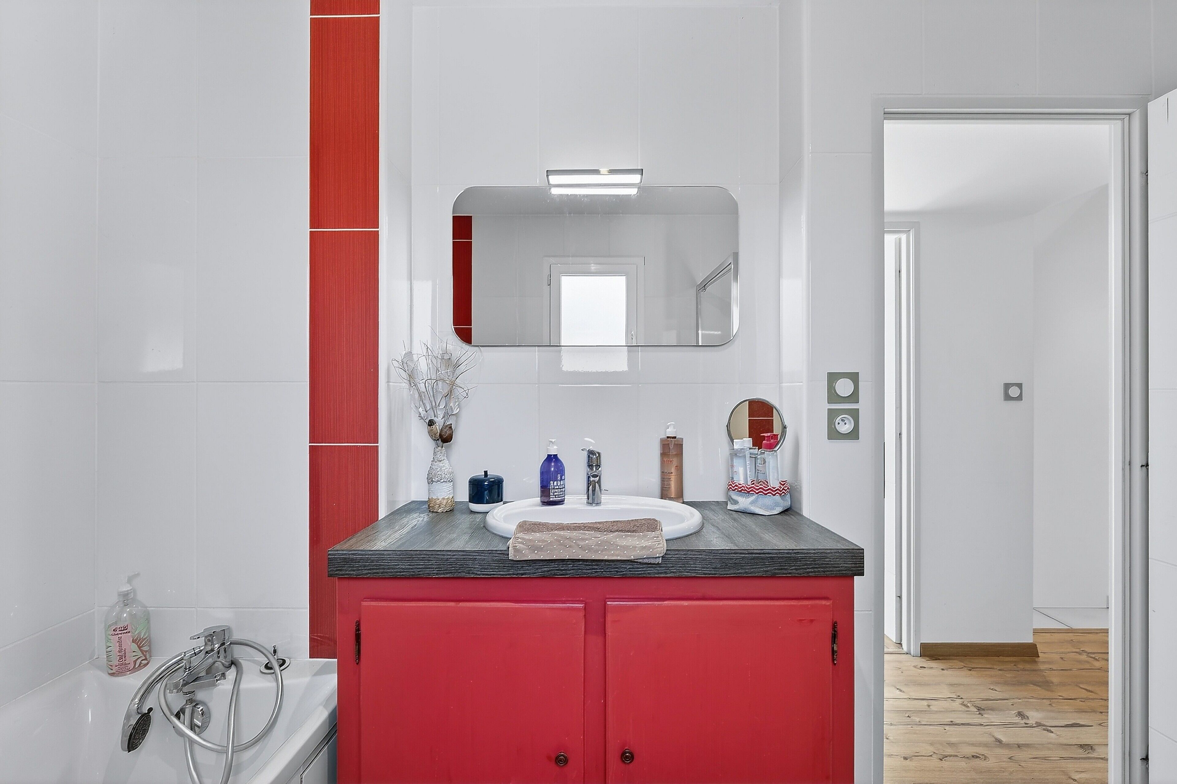 Ein Badezimmer mit einem weißen Waschbecken, roten Schränken, einem Spiegel und einer Dusche.