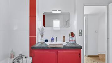 Ein Badezimmer mit einem weißen Waschbecken, roten Schränken, einem Spiegel und einer Dusche.