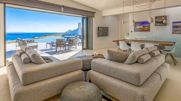 Ein modernes Wohnzimmer mit einem großen Schiebeglasfenster, das auf einen Balkon mit Pool und Meerblick führt.