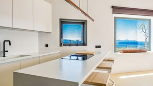 A modern kitchen with a central island, a window with a view, and built-in cabinets. - Paros Villa Skylines Estate I (Paros)