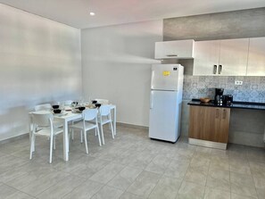 A modern kitchen with white cabinets, a white refrigerator, and a dining table set for four. - Safir Spacious Apartment in Safsaf, La Marsa (La Marsa)