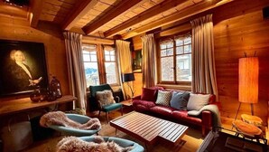 Ein gemütliches Blockhaus-Interieur mit einer Couch, Sesseln, einem Tisch und einem Kamin.