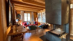Ein gemütliches Blockhaus-Interieur mit Holzbalkendecke, Kamin, einem roten Sofa und blauen Sesseln.