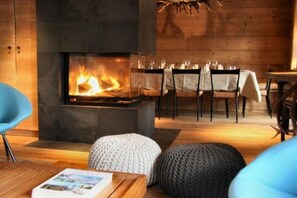 Une pièce chaleureuse avec une cheminée, des murs en bois et un coin repas comprenant des chaises et une table.