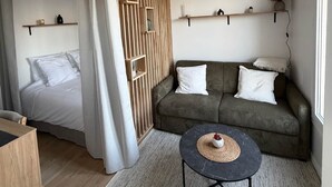 Ett modernt sovrum med en säng, en soffa, ett litet bord, en hängande lampa och inbyggda hyllor.
