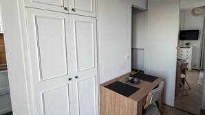 Ett kompakt kök med vita skåp, ett matbord i trä och en spegelbeklädd vägg som reflekterar rummet.