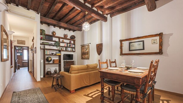 A cozy dining area with a wooden table and chairs, a sofa, and a bookshelf filled with books and decorative items. - Apartments Florence - Nido Fiorentino (Florence)