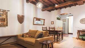 A cozy living room with a sofa, wooden coffee table, and a dining table with chairs. A mirror hangs on the wall, and there is a wooden beam ceiling. - Apartments Florence - Nido Fiorentino (Florence)