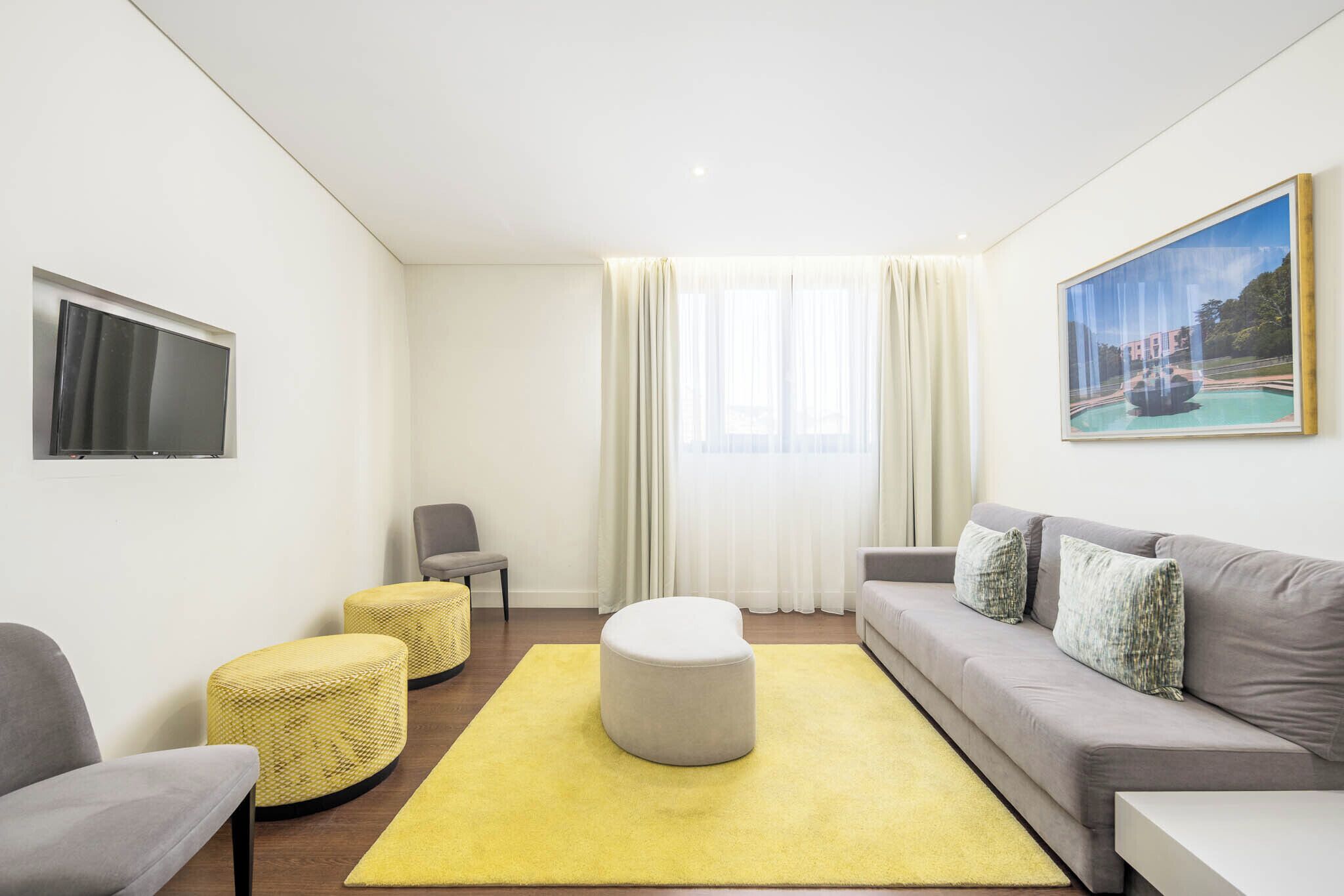 Una sala de estar moderna con sofá, reposapiés y sillón, un televisor de pantalla plana y un cuadro de una fuente.