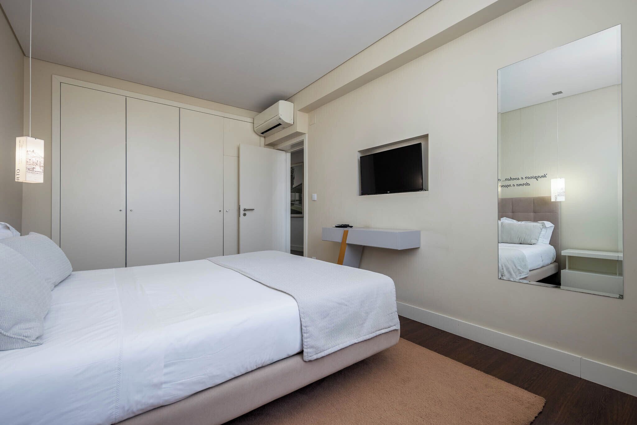 A bedroom with a bed, a TV, a mirror, and a wardrobe.