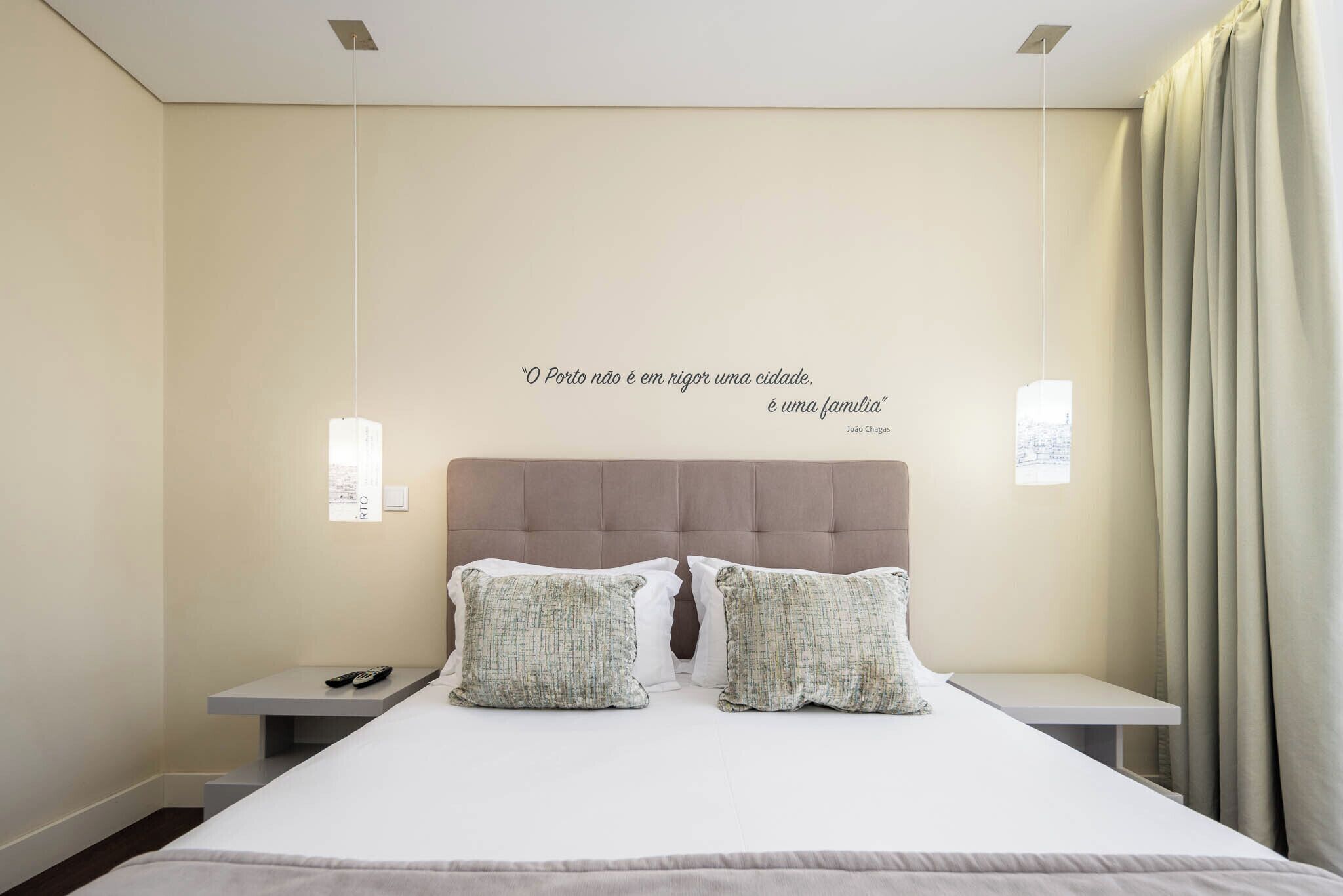 Ein Schlafzimmer mit einem Bett, zwei Nachttischen, einer Wandleuchte, einem Zitat und einem Fenster mit Vorhängen.