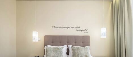 Une chambre à coucher avec un lit, deux tables de chevet, une lampe fixée au mur, une citation et une fenêtre avec des rideaux.