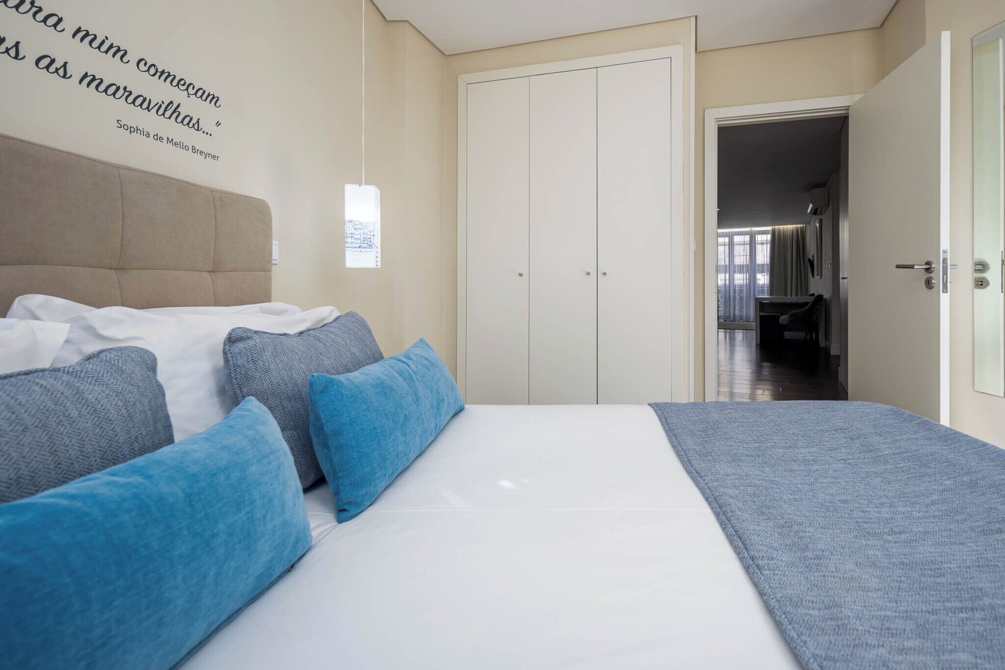 A bedroom with a bed, pillows, a wardrobe, and a wall quote.