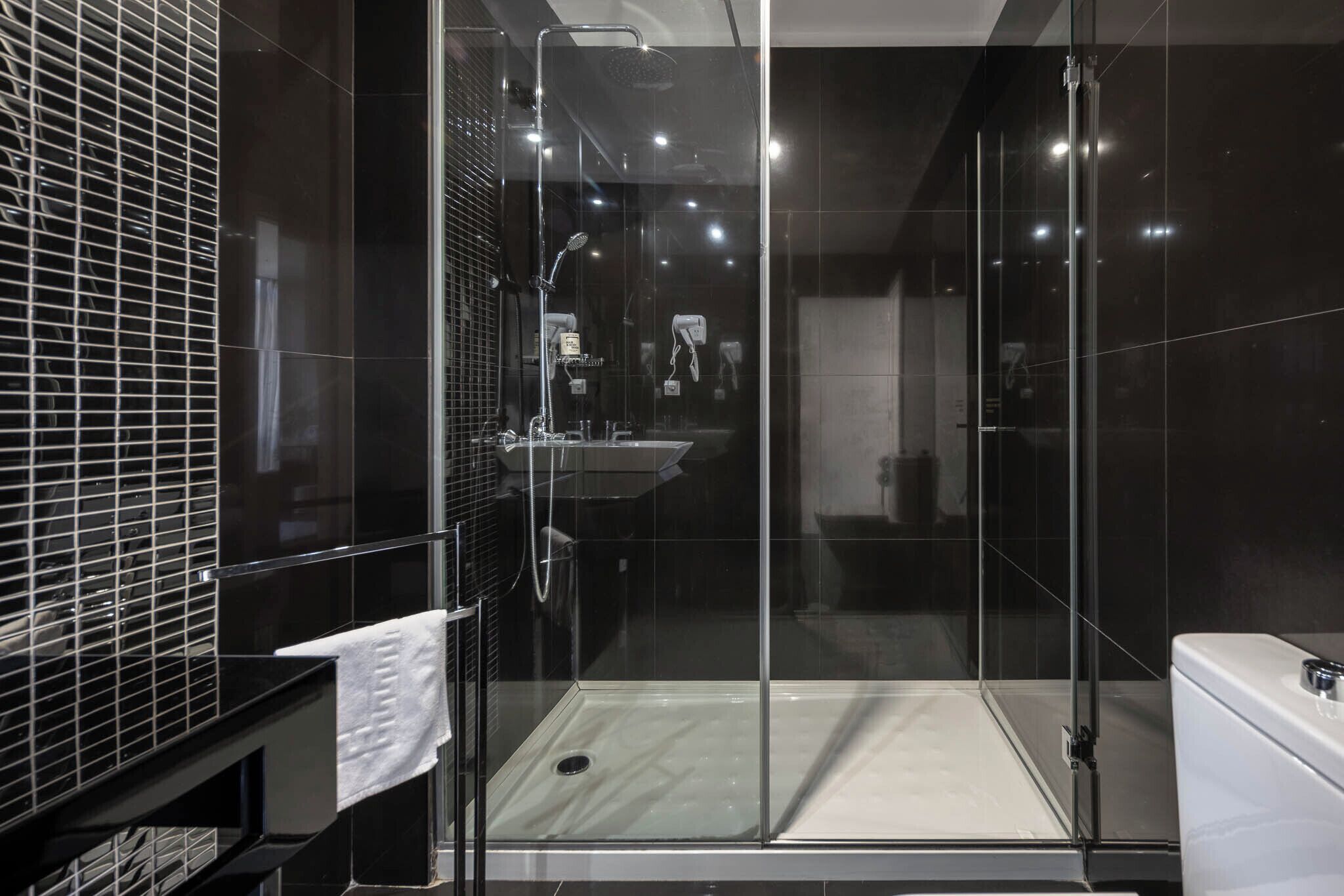 A modern bathroom with a glass shower enclosure, a white sink, and a black tiled wall.