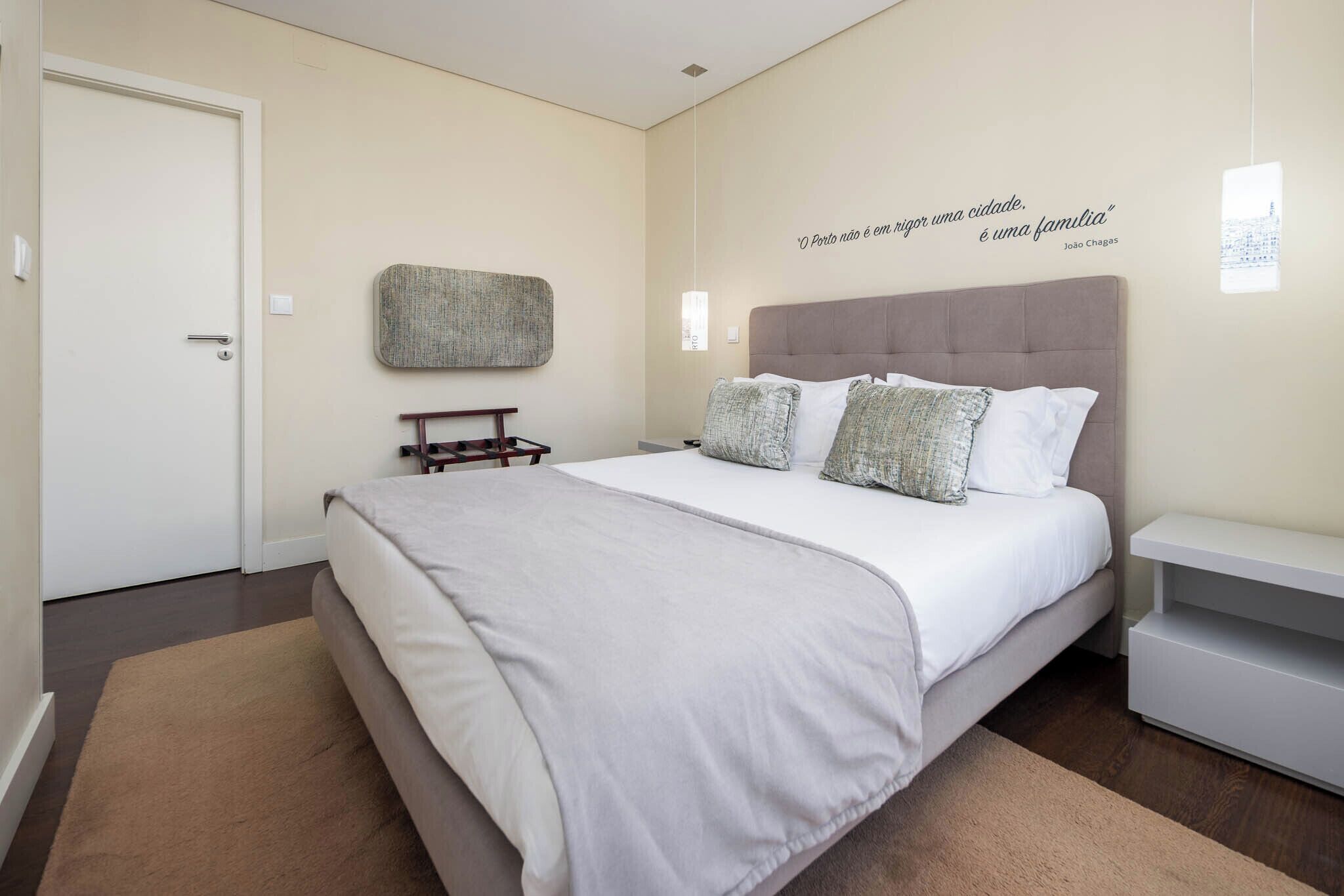 A bedroom with a bed, a bedside table, a nightstand, a wall-mounted light, and a quote on the wall.