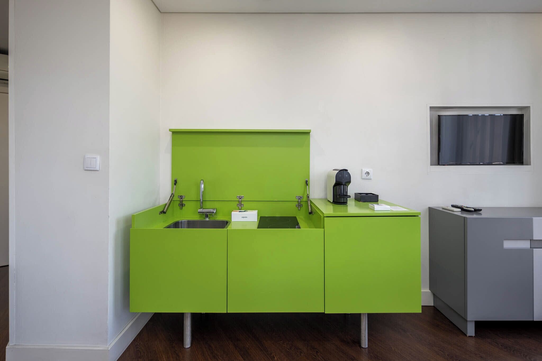 A modern kitchen with green cabinetry, a built-in sink, and a coffee machine.