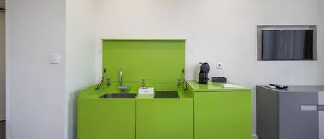 A modern kitchen with green cabinetry, a built-in sink, and a coffee machine.