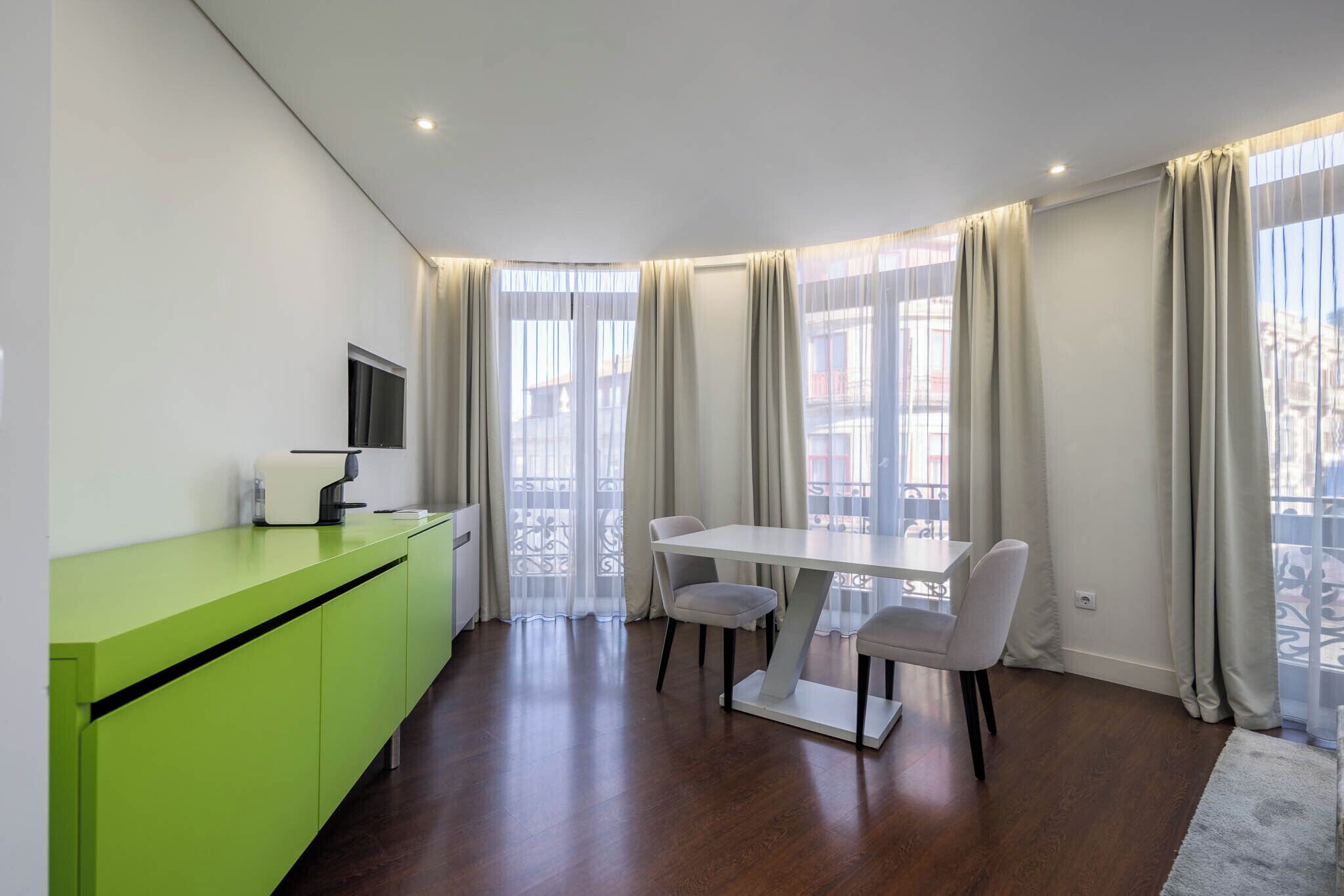 A modern kitchen with a green countertop, a dining table with chairs, and large windows with curtains.