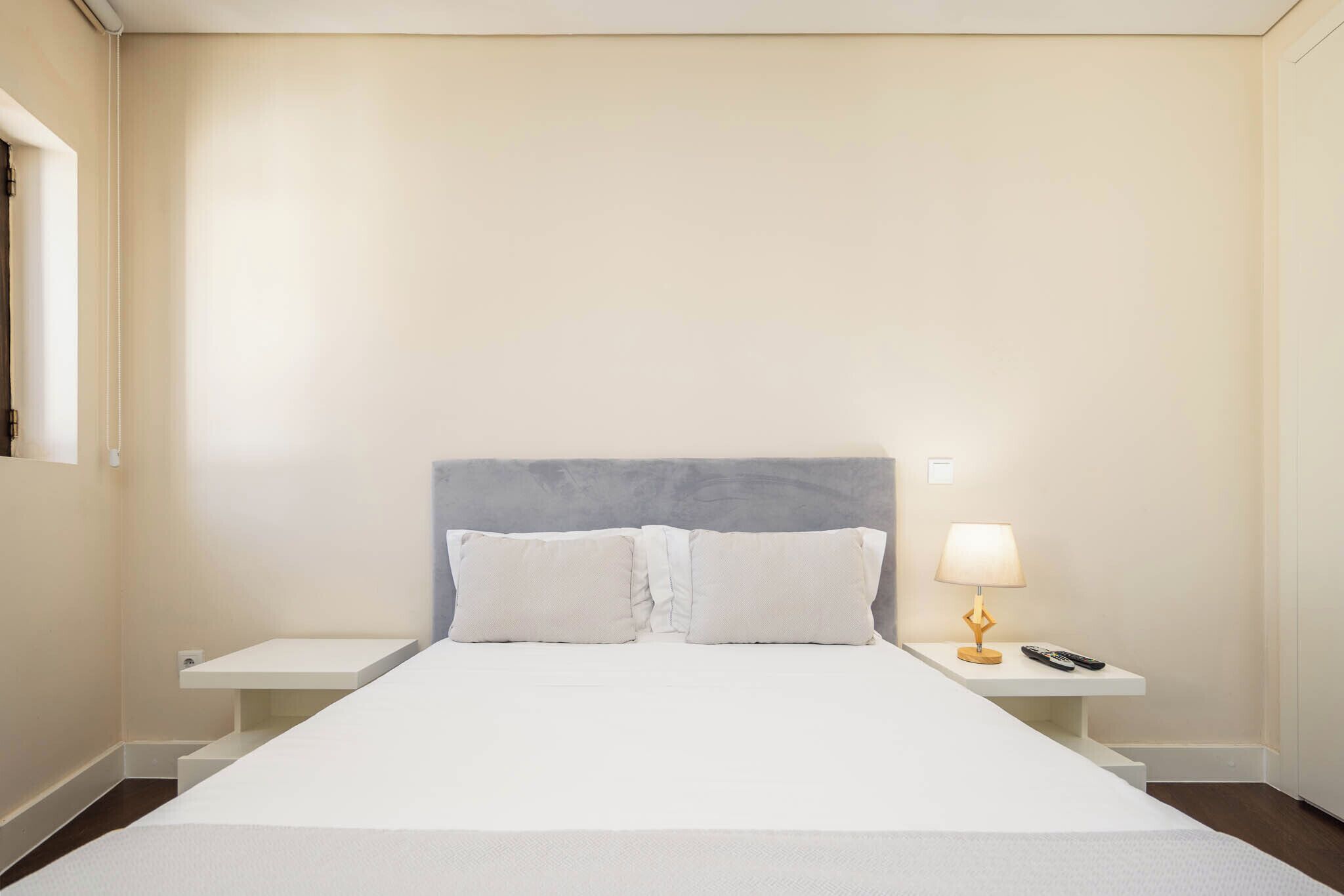 A hotel room with a bed, nightstands, a lamp, and a window.