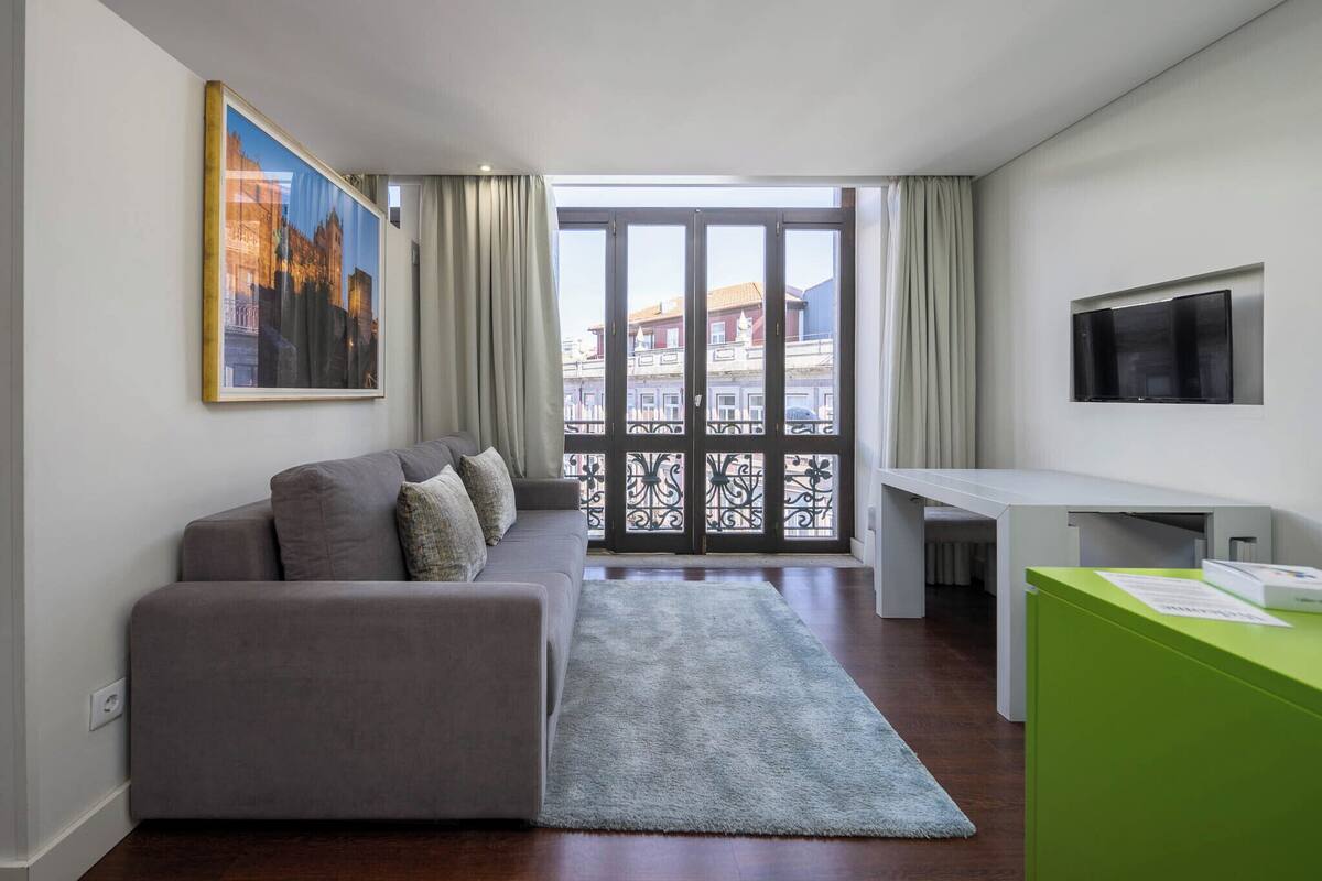 Una sala de estar moderna con sofá, escritorio, televisor y balcón con vista a la ciudad.