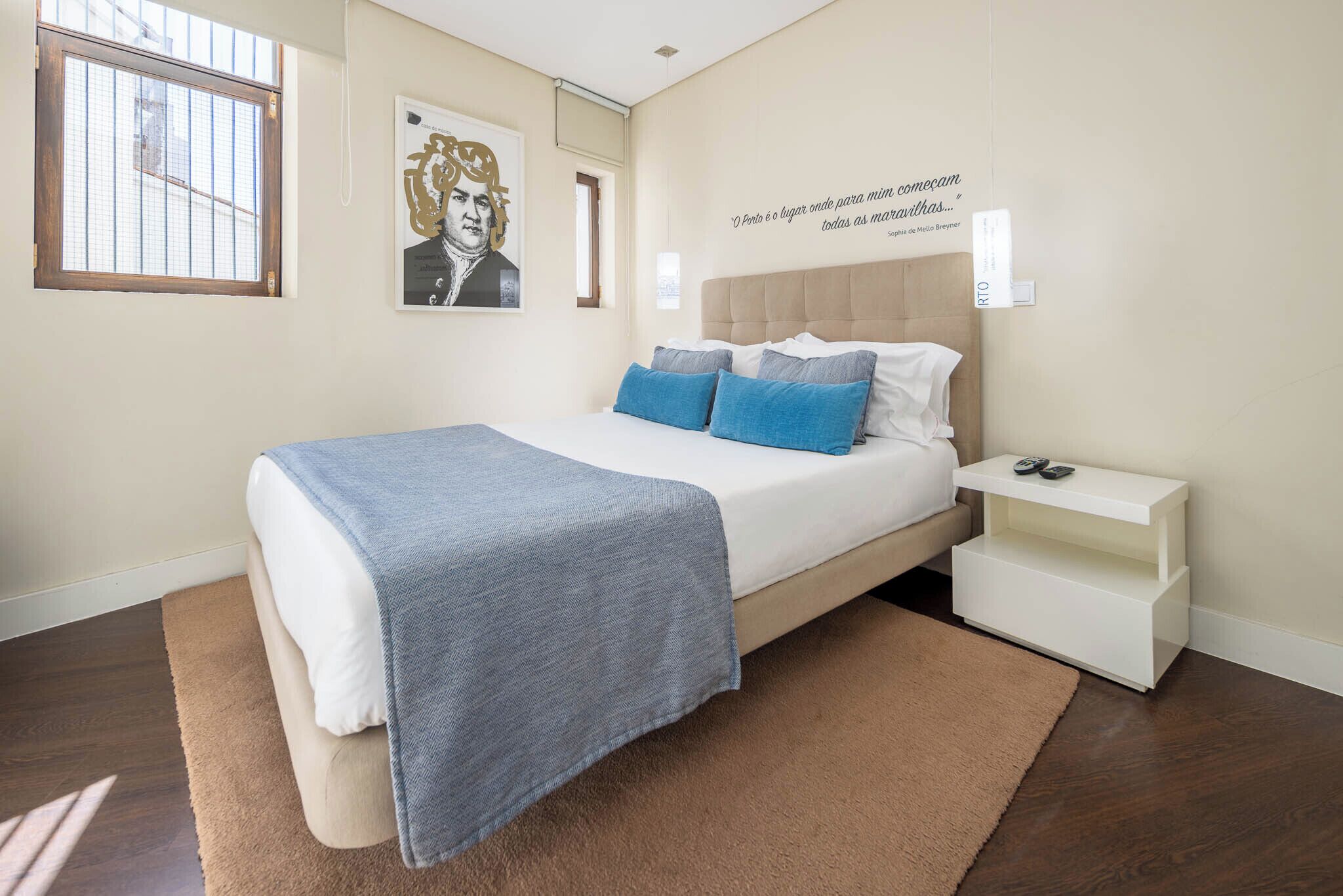 A bedroom with a bed, a nightstand, a window, and a poster on the wall.