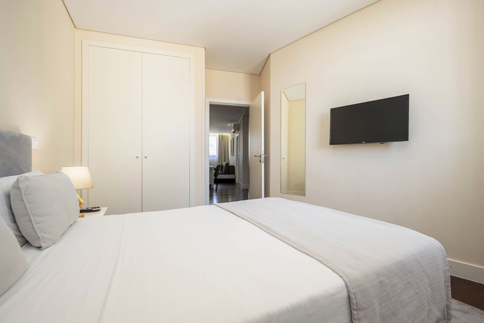 Une chambre à coucher comprenant un lit, une télévision, une armoire et une porte donnant sur une autre pièce.