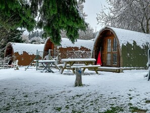A rustic cabin with a snow-covered roof and a wooden door. - Camping Le Pommier Rustique (Yvoir)