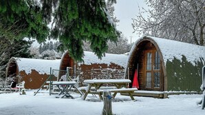 Un rustico chalet di legno con tetto innevato, una porta in legno e una panchina di fronte.