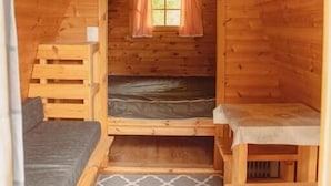 Una piccola baita di legno con un letto a soppalco, un letto singolo e una panca.