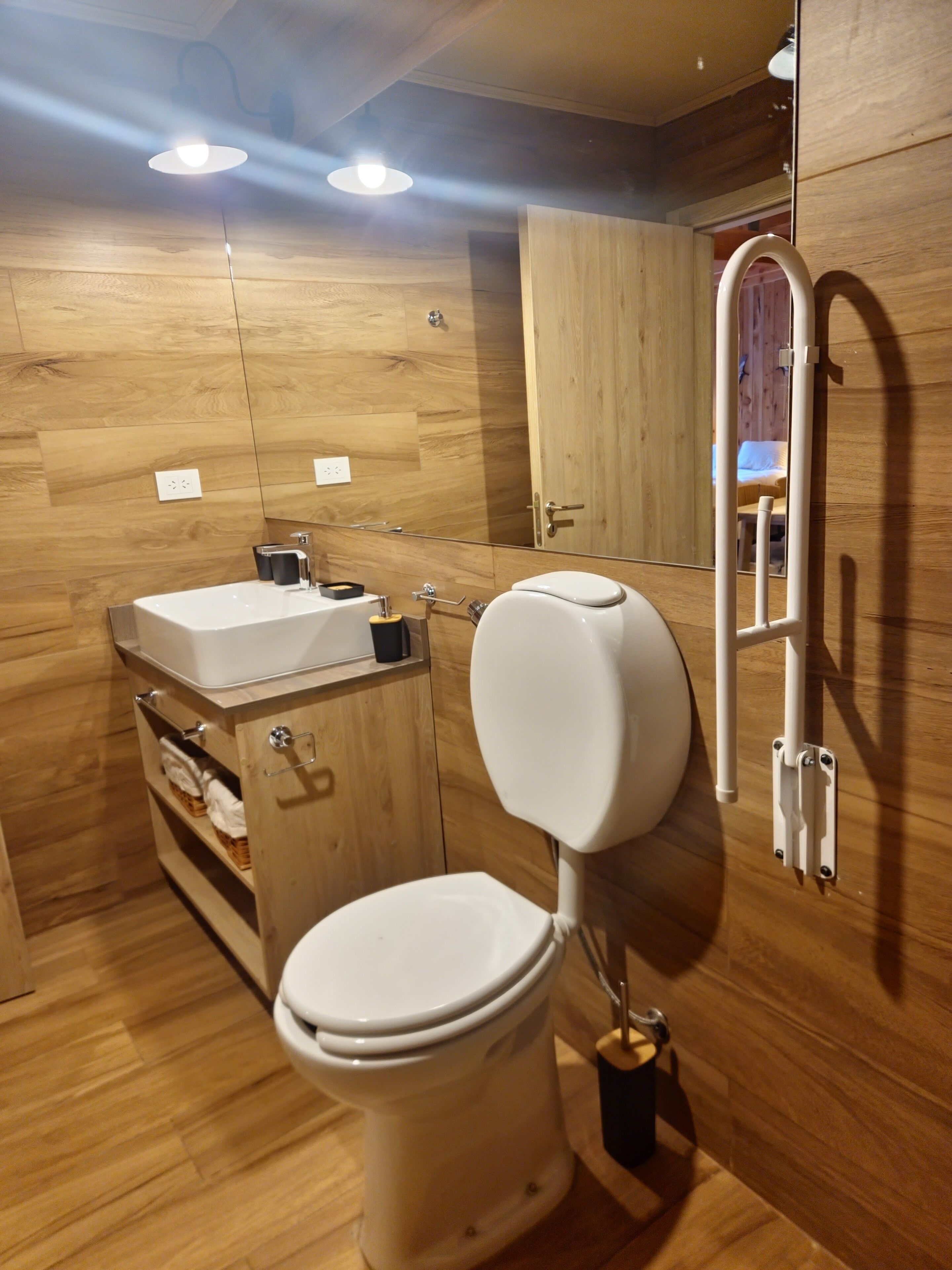 Un baño moderno con suelo de madera, un inodoro blanco, un lavabo y un espejo.