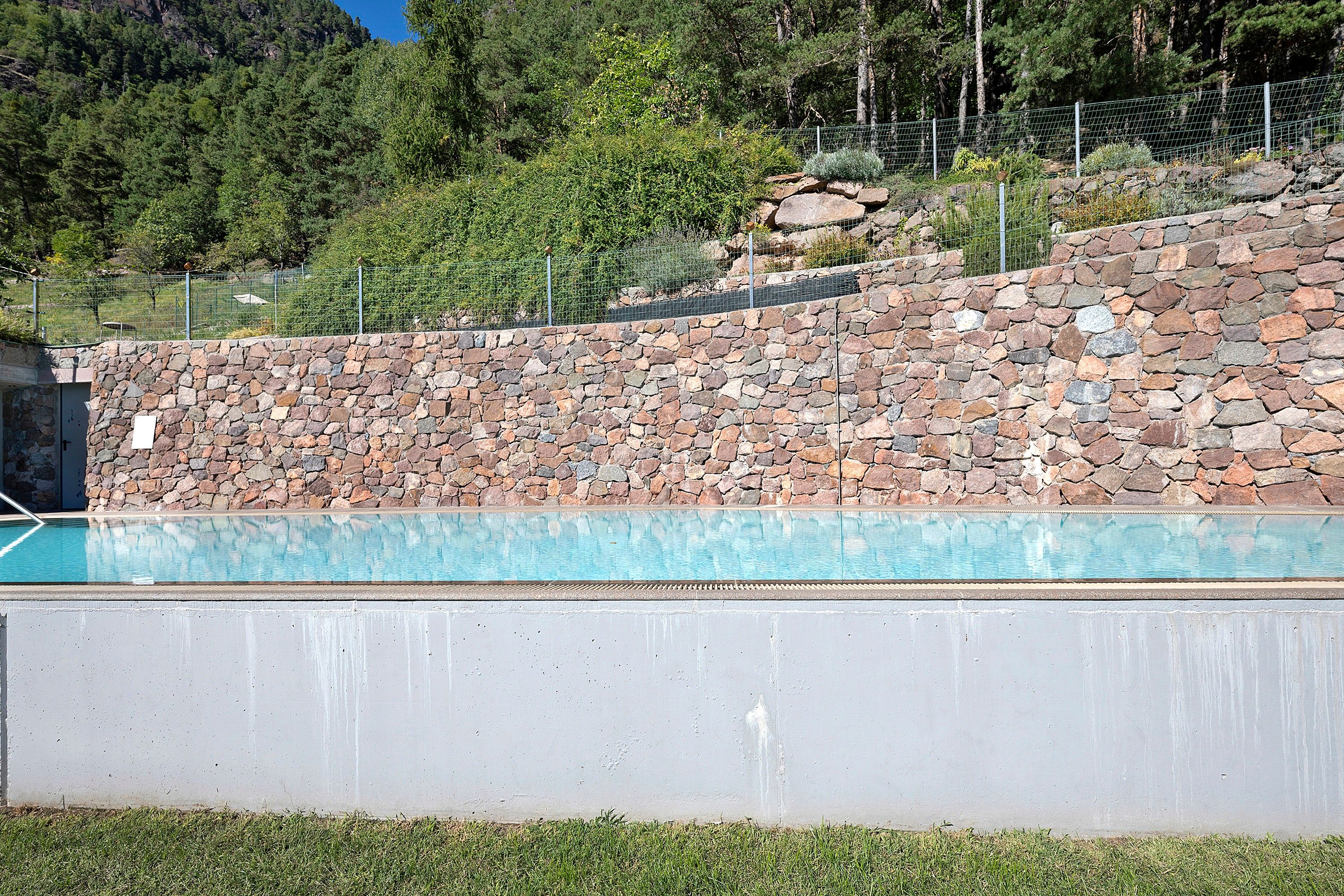 Ein Pool mit Steinmauer und Metallzaun in einer natürlichen Umgebung.