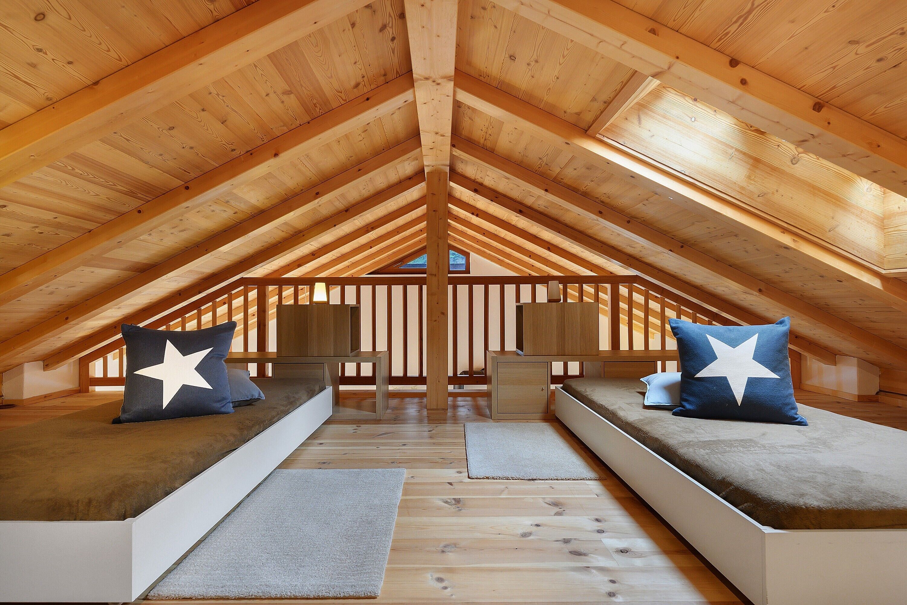 An attic bedroom with a sloped wooden ceiling, two built-in beds with star-patterned pillows, and a small table in the center.