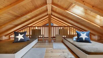 An attic bedroom with a sloped wooden ceiling, two built-in beds with star-patterned pillows, and a small table in the center.