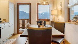 Un comedor con una mesa, sillas, una botella de vino y vistas a montañas a través de las ventanas.