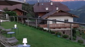 Una casa con balcón, césped con sillas de descanso y vistas a la montaña.