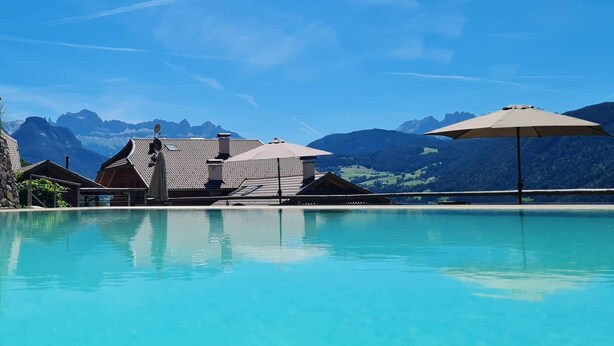 Una piscina cristalina con montañas al fondo, edificios de madera y un paraguas grande.