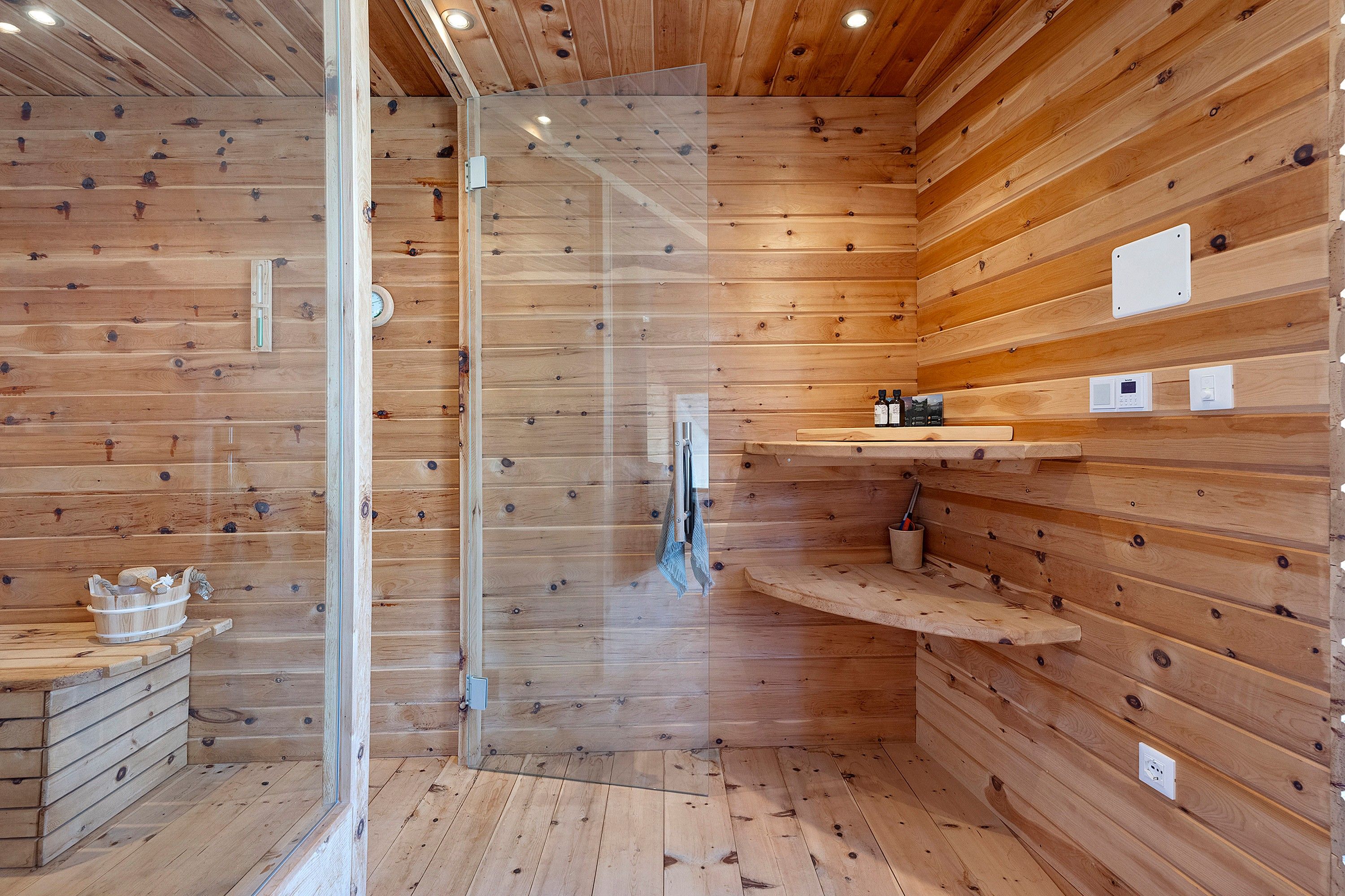 A wooden interior with a glass shower enclosure, wooden shelves, and a small wooden cabinet.