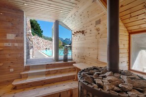 A wooden interior with a stone wall, a fireplace, and a view of a pool and mountains. - Apartment 'Felixdachl' with Mountain View, Shared Pool and Wi-Fi (Renon)