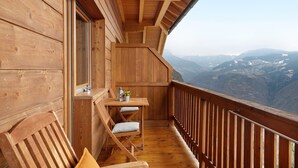 Un balcón de madera con una mesa y sillas, con vista a un paisaje montañoso.